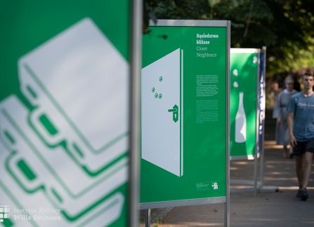 fotografia. wystawa Wyszehrad to ludzie na krakowskich plantach. ludzie przechadzają się pomiędzy plakatami ustawionymi w rzędzie wzdłuż alejki.